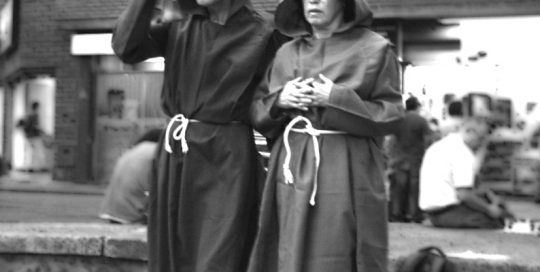 Two performers dressed as monks walking through the street.