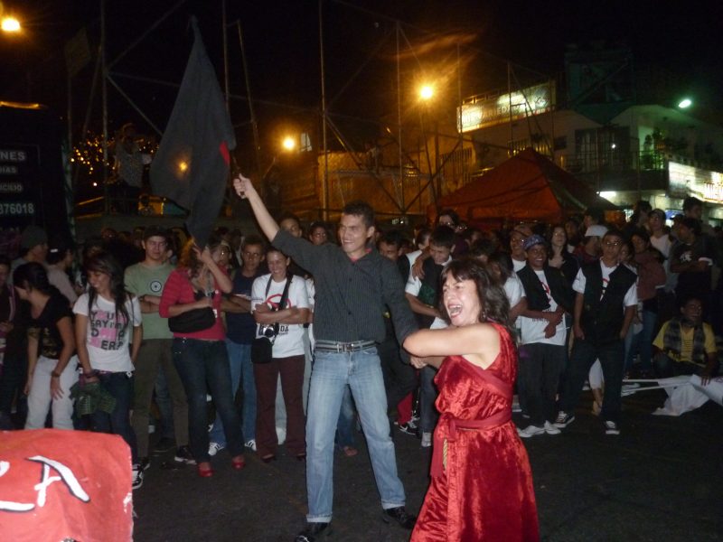 Nightime shot of a large crowd watching and laughing as two people dance in the street.