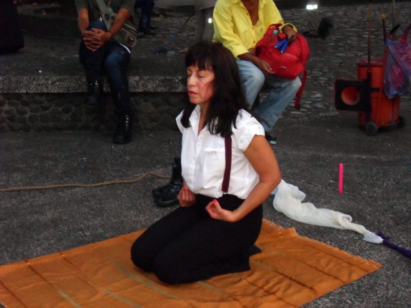 A woman kneeling on the ground holding her hands next to her in meditation.