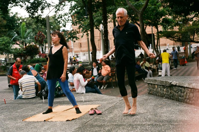 Two performers in the street, one in a pose while one jumps rope.