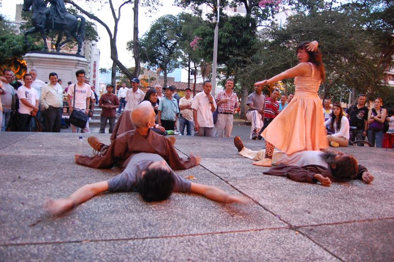 Four performers on a sidewalk, two are laying on the ground will the other two sit atop them.