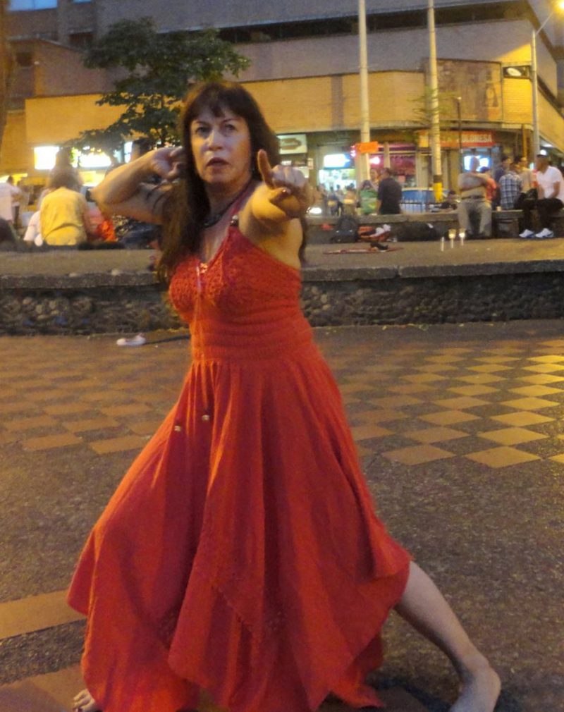 A woman in a red dress in a dance pose on the sidewalk.