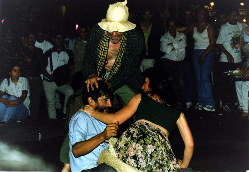 Three performs dancing in the street in the middle of the night with a crowd of people behind them.