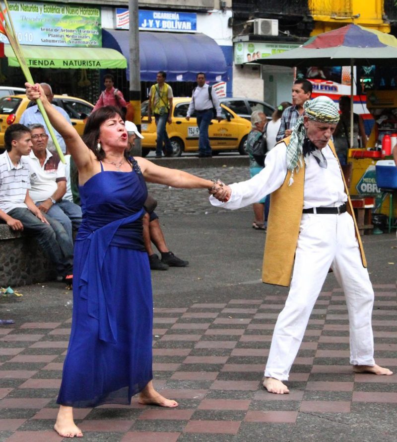 An older man and a woman perform on the sidewalk in a dramatic pose with their feet apart.