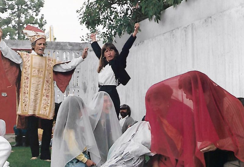 Two performers stand with their arms up with people sitting infront of them with a blanket draped over them.