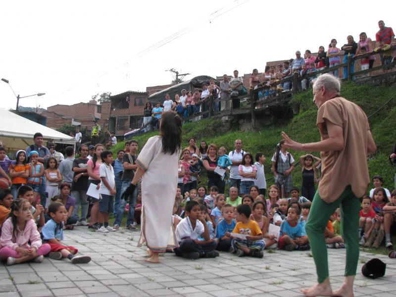 A man and woman in cosume perform for children sitting infront of them.